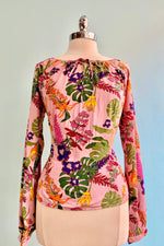 Pink blouse with a tropical plant print in rainbow colors.  This top has a blousson sleeve and a smocked back panel.  This is a pullover top with an elasticized neckline and does not have any additional closures.    100% Viscose